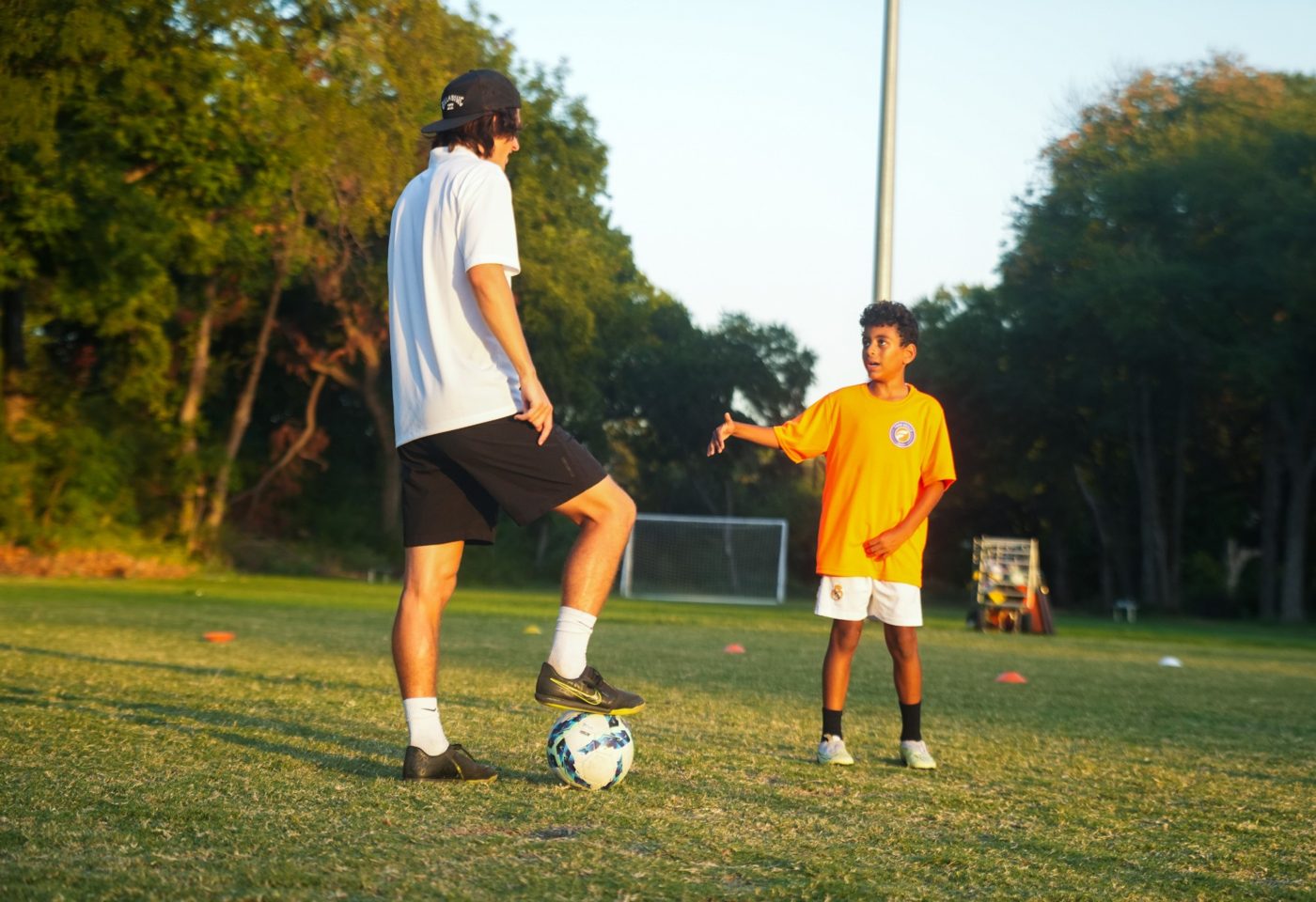 A coach with his foot on the ball talks with a young player