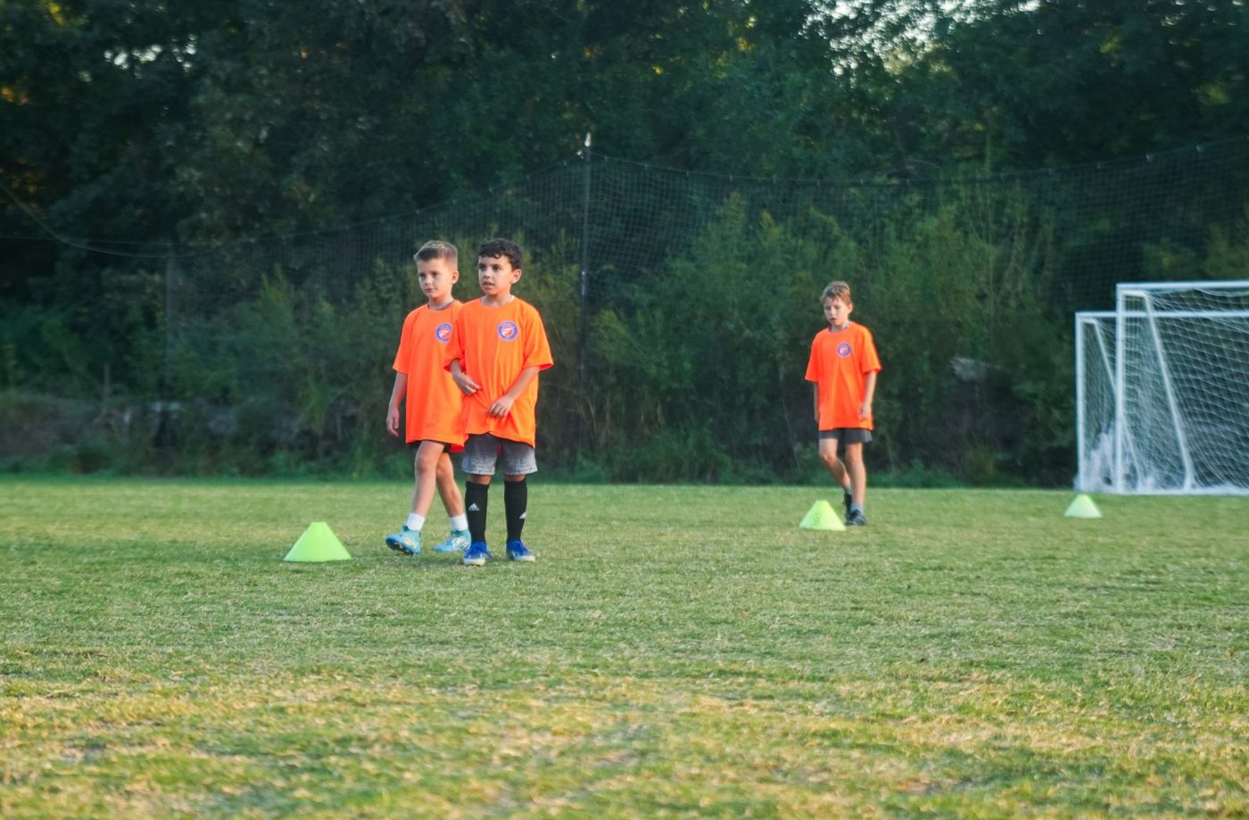 Three young players in orange Foro shirts walking between training cones