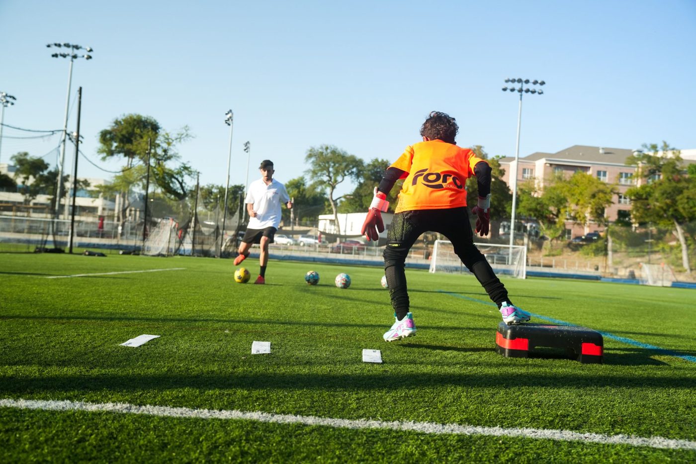 A young goalkeeper in a Foro jersey faces a coach during a drill