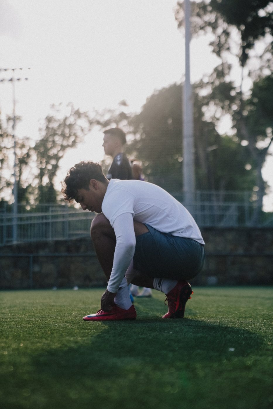 An adult player ties his cleat on the field at sunset