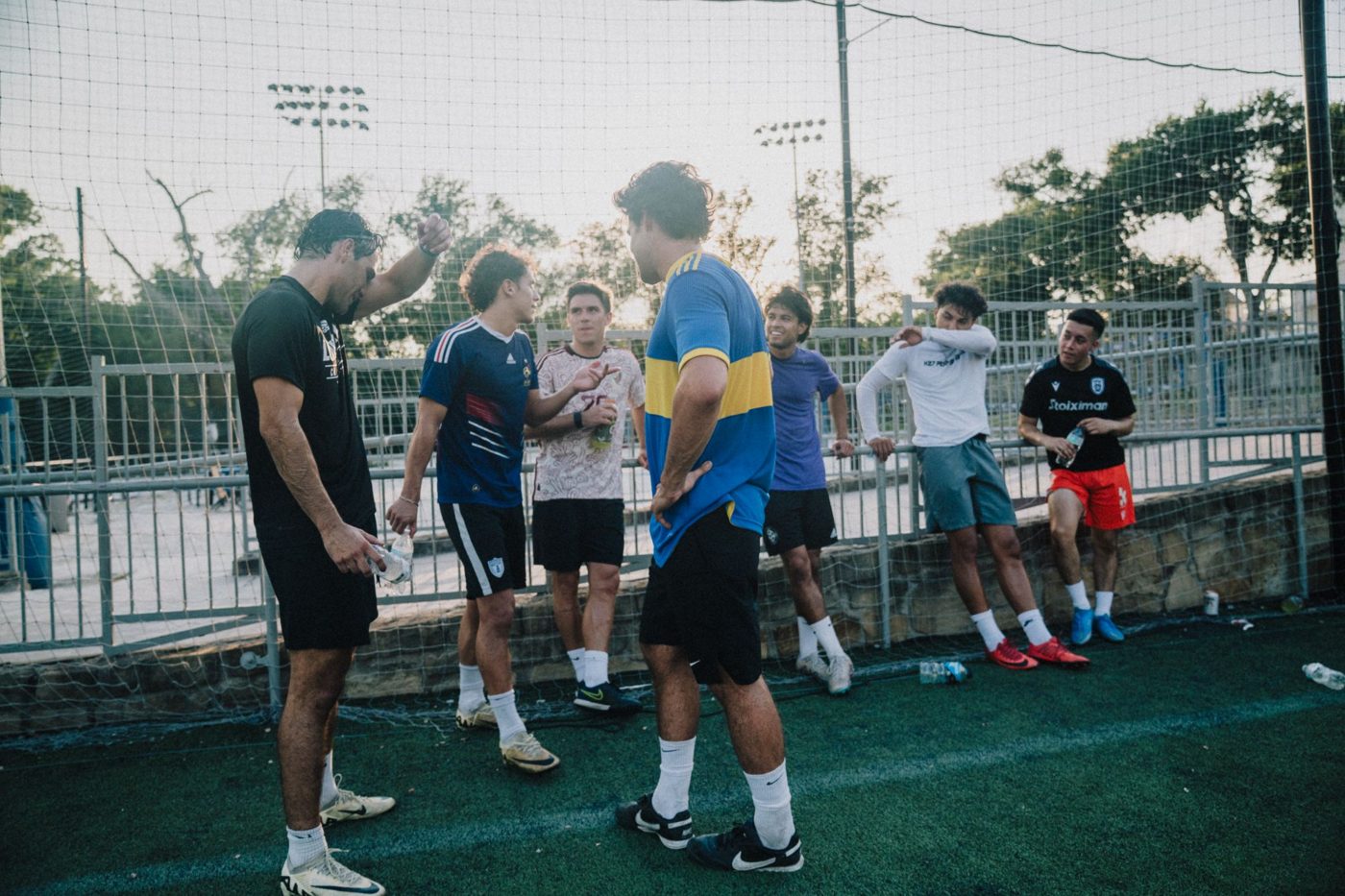 Adult players chat and cool off by the fence after a game