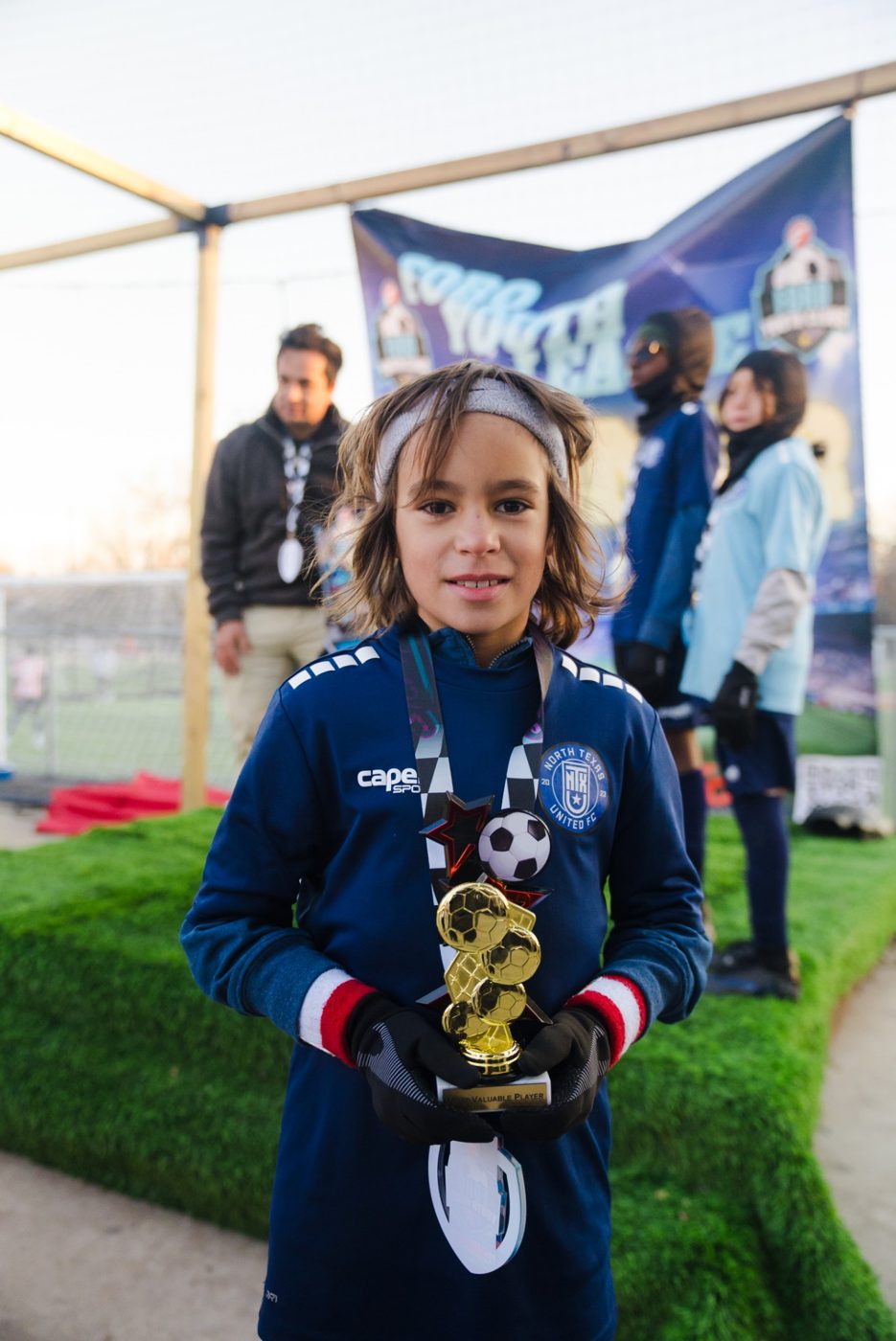 A young player holds a Most Valuable Player trophy and a medal at the Foro Youth League finals